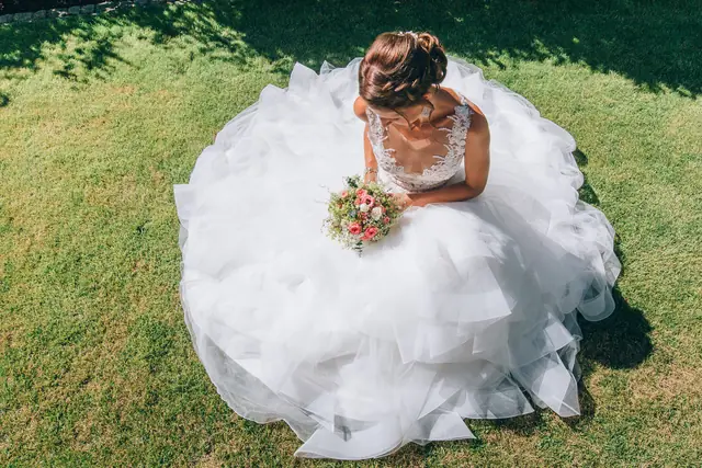 Braut sitzt im ausladenden Kleid auf einer Wiese